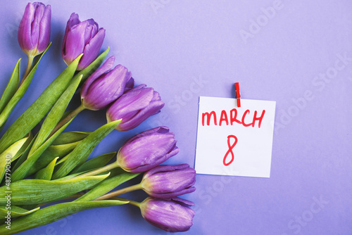 Purple bouquet of flowers tulips background with a note March 8 on veri peri background.