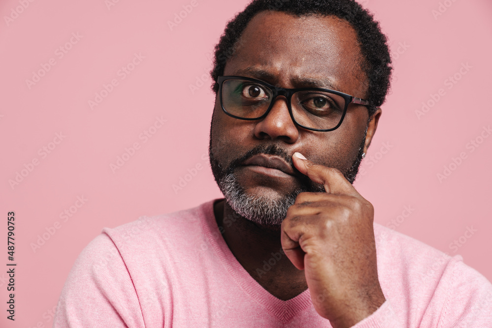 Black puzzled man in eyeglasses thinking while looking at camera Black puzzled man in eyeglasses thinking while looking at camera