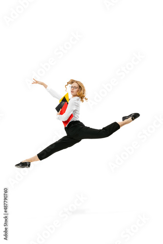 Dynamic portrait of young pretty girl wearing business style clothes jumping with folders isolated on white background. Finance, ballet, art, business, beauty concept.