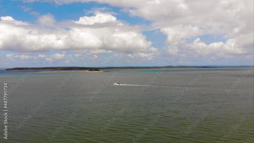Fly over of a small boat slowly sailing through the sea towards tropical waters whilst small islands sit on the horizon under huge, fluffy, white clouds Fly over of a small boat slowly sailing through the sea towards tropical waters whilst small islands sit on the horizon under huge, fluffy, white clouds