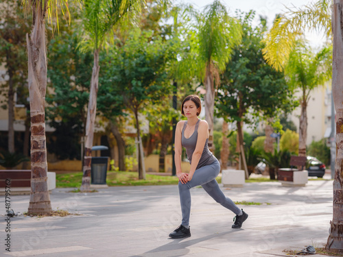 outdoor sports, workout and wellness concept. asian young strong, confident woman in sportive clothes in green park warming up before jogging outdoors, leg stretching before running.
