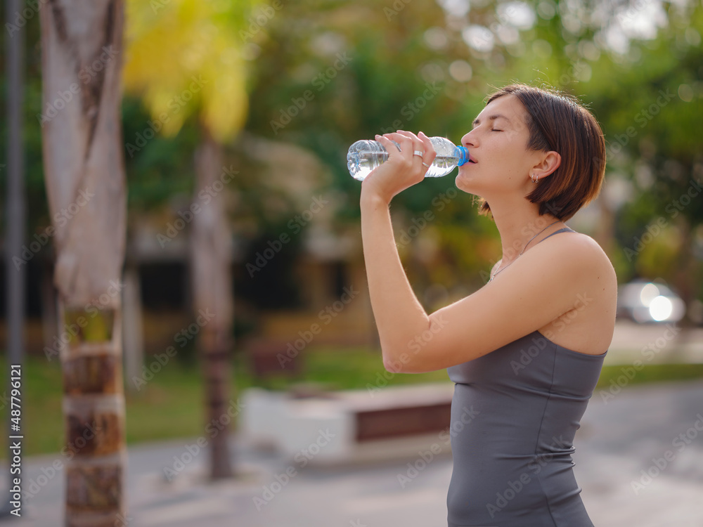 outdoor sports, workout and wellness concept. asian young strong, confident woman in sportive clothes in green park drinking water after workout, feeling of thirst. outdoor sports, workout and wellness concept. asian young strong, confident woman in sportive clothes in green park drinking water after workout, feeling of thirst.