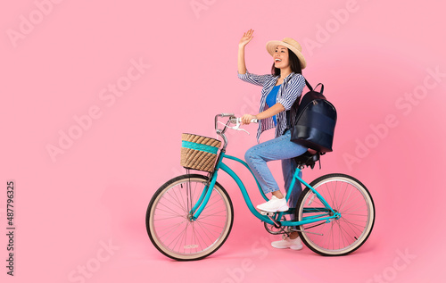 Excited asian woman riding retro bicycle with wicker basket © Prostock-studio