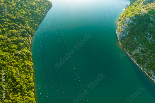 Oyster farm surrounded by high green mountains of Istria peninsula. Waters of Lim bay flowing into Adriatic sea at bright sunlight. Aerial panorama