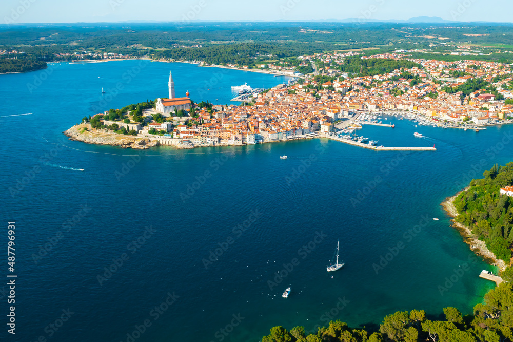 Fototapeta premium Surroundings of Rovinj town with St. Euphemia church high tower on hill. Croatian town houses surrounded by green forests of peninsula. Aerial panorama