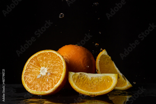 Water pours on oranges on a black background. Spray of water on cut oranges. Refreshing fruit