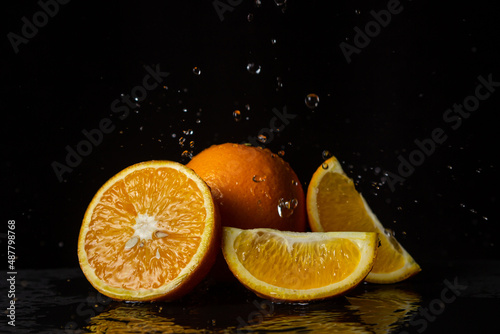 Fototapeta Naklejka Na Ścianę i Meble -  Water pours on oranges on a black background. Spray of water on cut oranges. Refreshing fruit