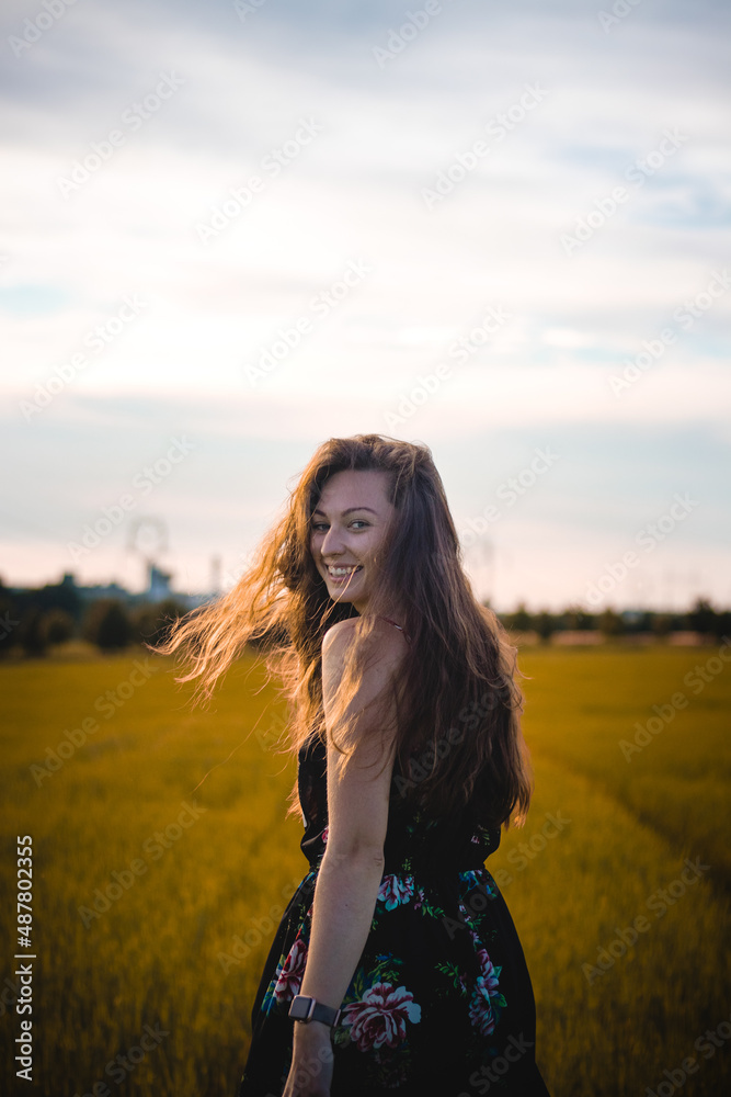 Breathtaking brunette model with a natural wide smile in a dark summer floral dress walks through the tall grass, her wavy dark hair flying. Candid portrait real adult woman. Czech republic, Europe Breathtaking brunette model with a natural wide smile in a dark summer floral dress walks through the tall grass, her wavy dark hair flying. Candid portrait real adult woman. Czech republic, Europe