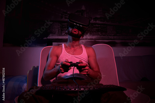 a thirty-year-old gamer in vr glasses with a keyboard and a joystick in his hands plays computer games, gets angry, feels indignation, various emotions. view from the TV side