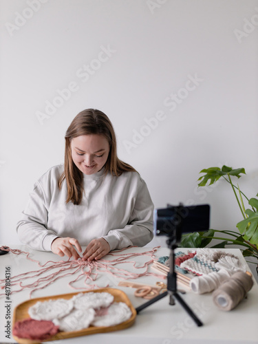 Woman record new videovlog in living room. Puts smartphone on tripod girl make online live stream, lead webinar distant chat, modern tech, video concept. Handmade macrame in work process. Female hobby photo