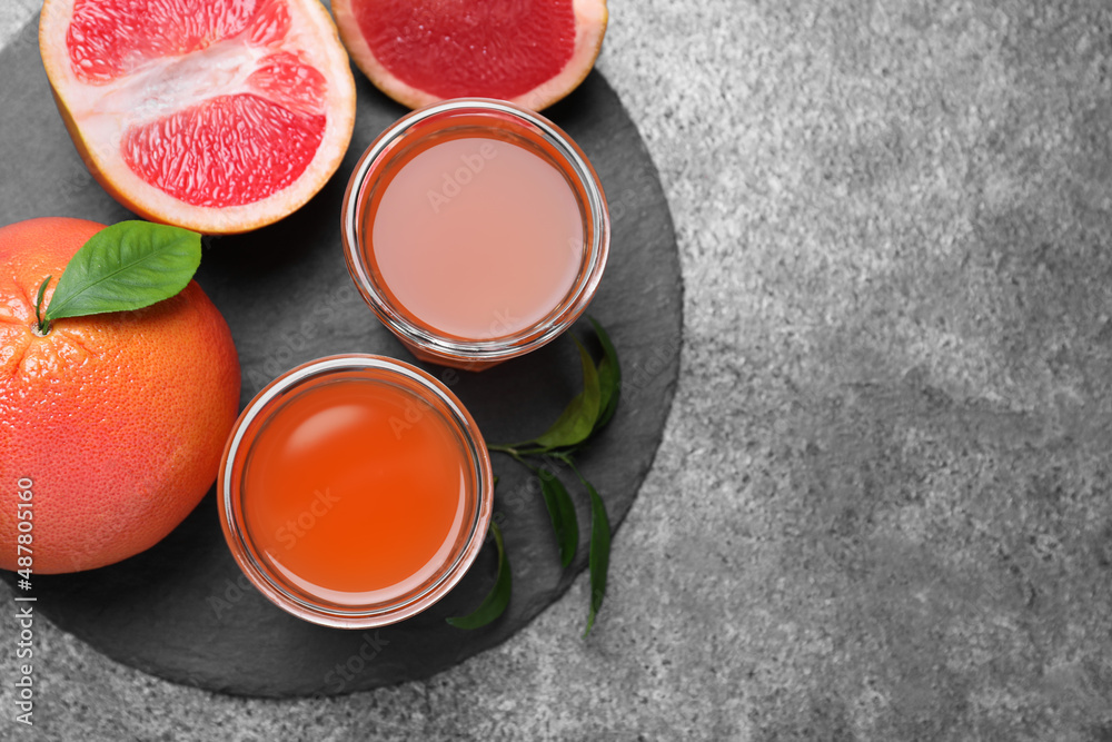 Tasty freshly made grapefruit juice and fruits on grey table, flat lay. Space for text