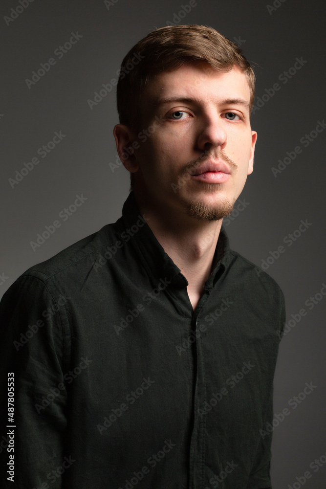 Portrait of young blond european man with short beard and mustache isolated on dark grey in black shirt