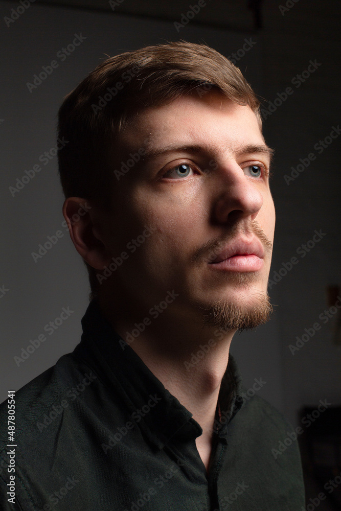 Portrait of young blond european man with short beard and mustache isolated on dark grey in total black outfit