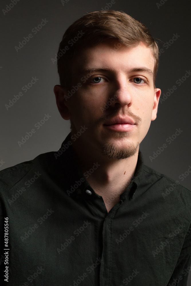Portrait of young blond european man with short beard and mustache isolated on dark grey with shadow on his face Portrait of young blond european man with short beard and mustache isolated on dark grey with shadow on his face