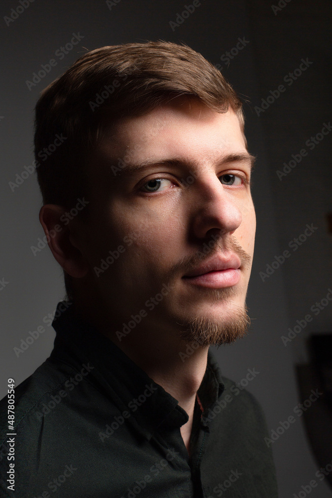 Fototapeta premium Portrait in shadow of young blond european man with short beard and mustache isolated on black