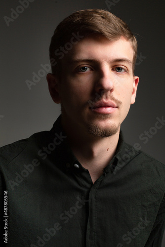 Portrait of young blond european man with short beard and mustache isolated on dark grey with shadow on his face
