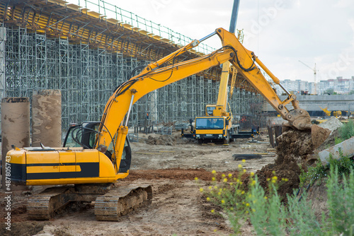 Big yellow excavator digs the ground with the front bucket at the construction site