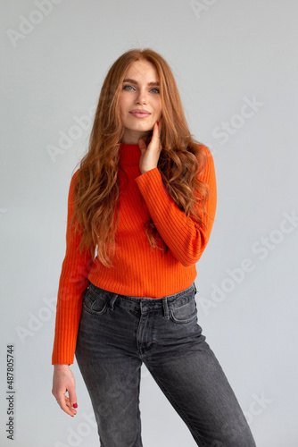 Pretty woman with long red hair in orange jumper isolated on light grey