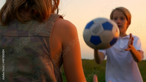 Brother and sister playing ball in the backyard in the rays of the setting sun. Happy teenagers play together and smile at each other. Teenage children have a carefree childhood.