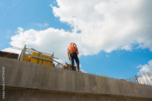 Builder in a hardhat and a vest on a concrete structure against the sky