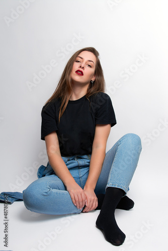 a girl with bright red lipstick, blue jeans and a black T-shirt sits on a white background.