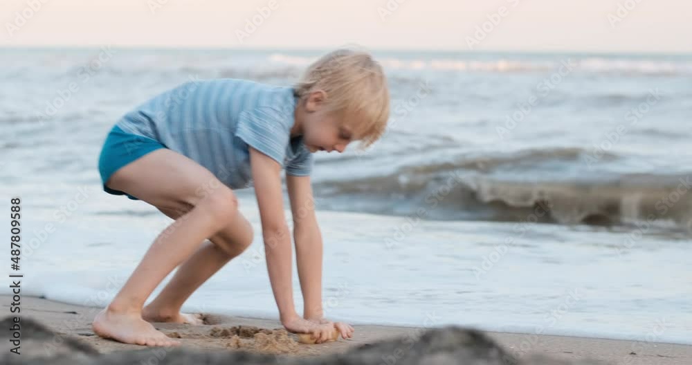 Boy is playing on the waters edge with sand. Child is fooling around on the beach. Holidays with children on the sea. Boy is playing on the waters edge with sand. Child is fooling around on the beach. Holidays with children on the sea.