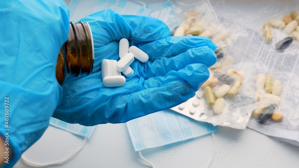 Fototapeta premium The doctor pours several white pills from a bottle into a gloved hand. The doctor prescribed a medicine to treat the disease of the coronavirus infection. A nurse puts out pills for sick patients.