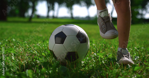 Fototapeta Naklejka Na Ścianę i Meble -  Closeup kid legs doing football tricks. Young player practice on green field.