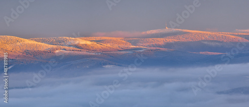 Czech mountain range High Jesenik with the highest peak of Praded immersed in the fog at sunset, view from the Polish peak of Czarna Gora in winter.