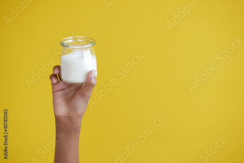 holding a jar of white sugar against yellow background 