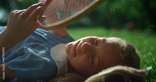 Dreamy girl lying on blanket touching racket strings in golden sunlight closeup