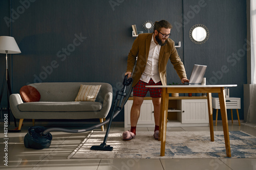 Glad multitasking businessman vacuuming and working online photo
