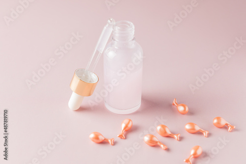 Transparent bottle of cosmetic or essential oil, aromatherapy with natural cosmetics. Pink capsules with cosmetic oil or serum for the faceon Pink background. photo