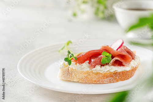 Open prosciutto sandwich with cream cheese, radish and microgreens on white background. Copy space
