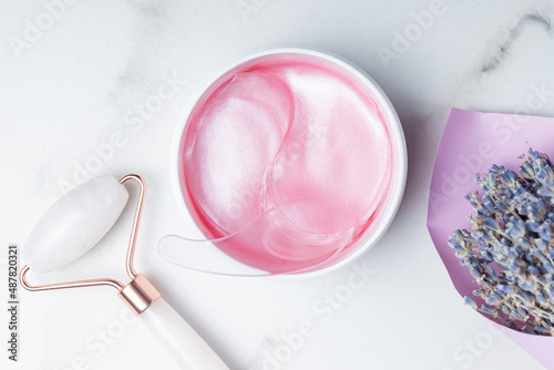 skin care home routine. Lavender putches for skin under eyes and roze quartz massage roller on marble background. top view.