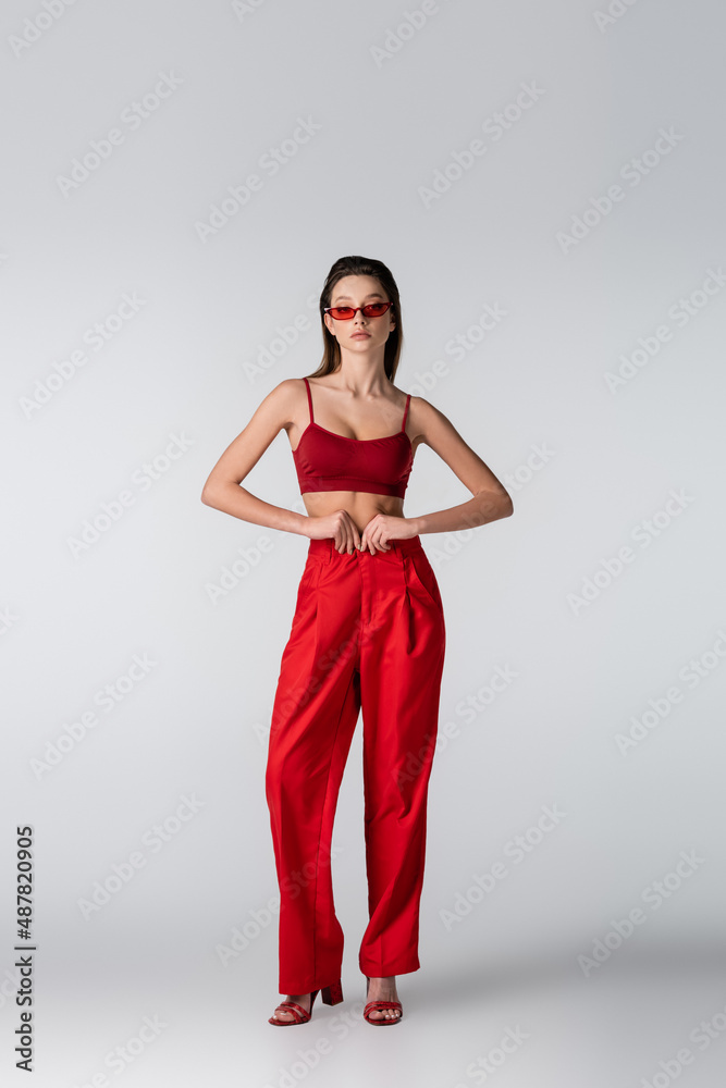 full length of young woman in sunglasses and red outfit posing on grey. full length of young woman in sunglasses and red outfit posing on grey.