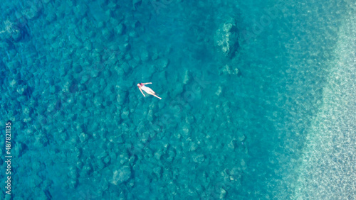 Young pretty woman in a white one piece swimsuit svimming on back in turquoise sea water. Woman lies on the water transparent water. Aeriale drone photo © Klemenso