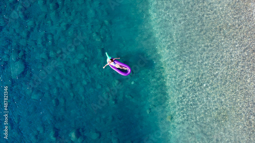 Young pretty woman in a white one piece swimsuit relaxing on a inflatable mattress in shape of big eggplant in turquoise sea water. Woman on air mtatress in transparent water. Drone top view © Klemenso