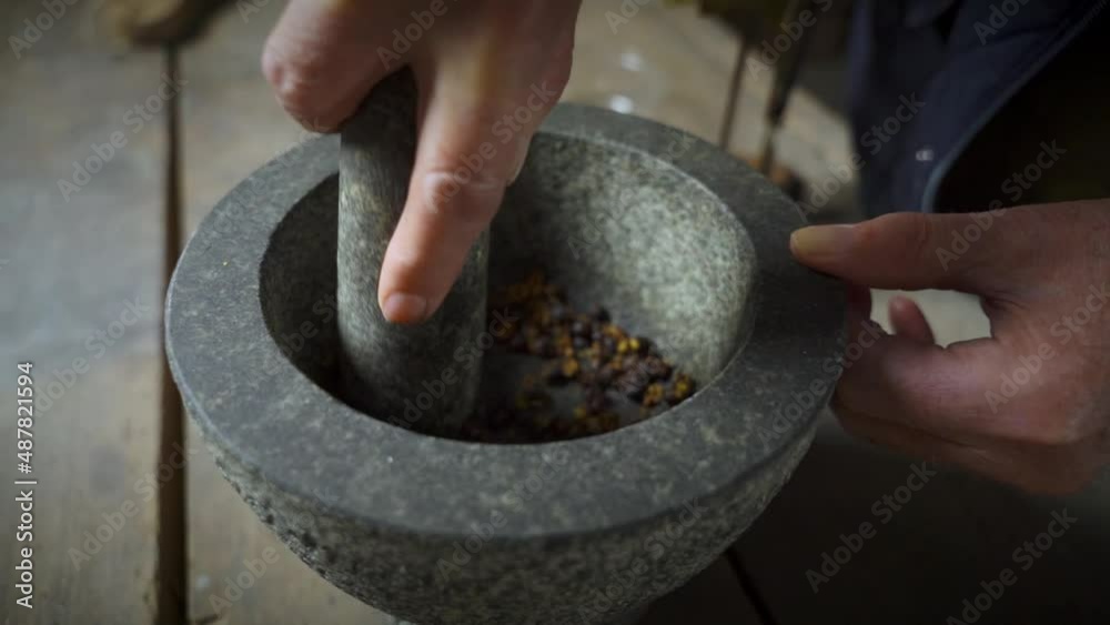 Old male hands triturating  juniper in stone mortar