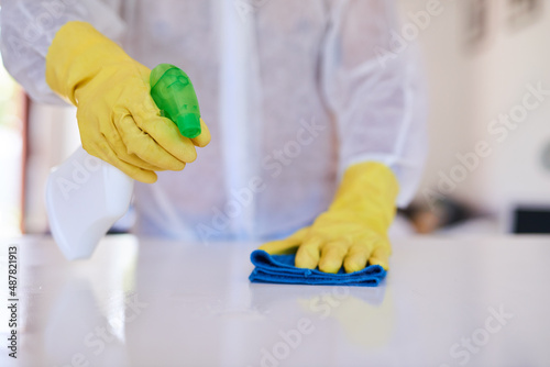 A cleaning professional sprays a kitchen counter with sanitiser