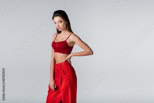 young model in red outfit posing with hand on hip isolated on grey.