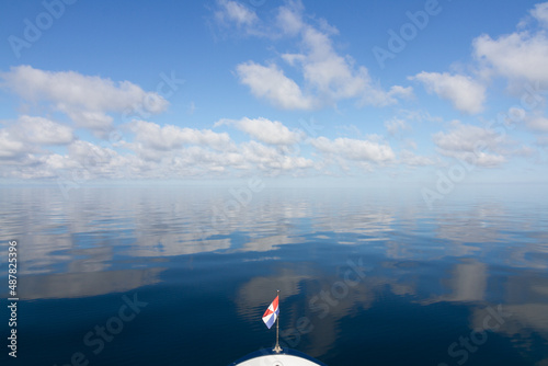 sailboat on a calm sea with blue sky and white clouds reflecting on the water