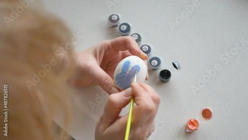 woman paints an Easter egg with paints. Easter bunny drawing on a white egg photo