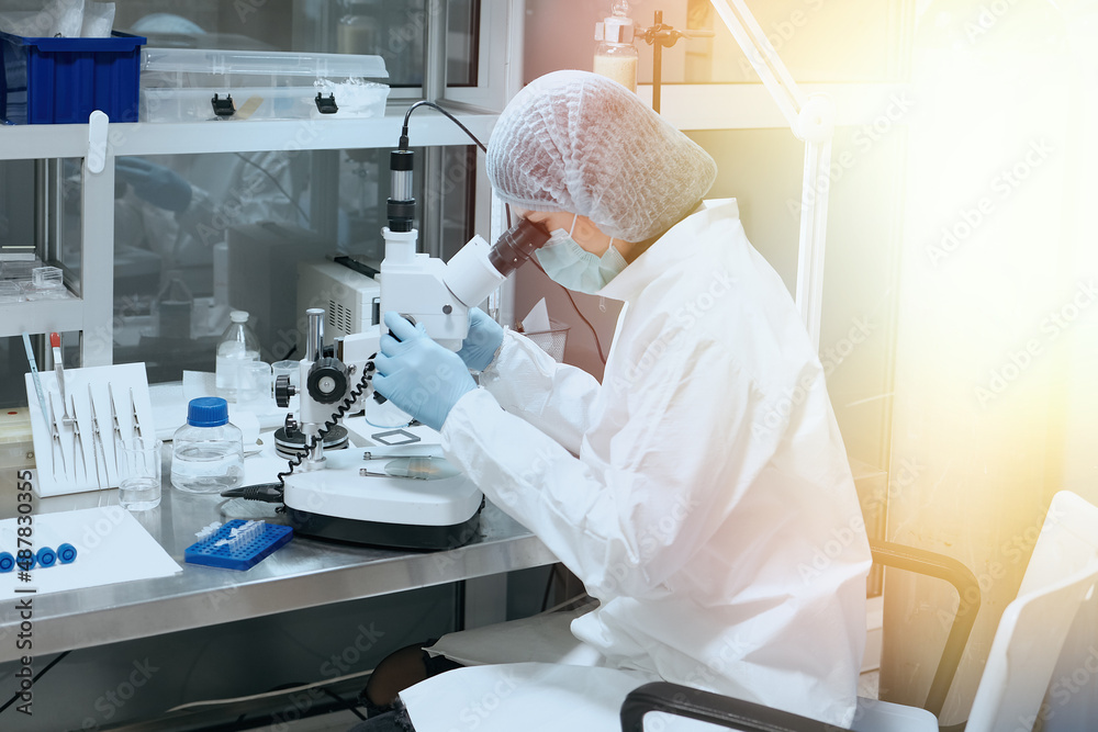 Medic or scientist looking through a microscope in a scientific medical laboratory. Biochemical research and medicine