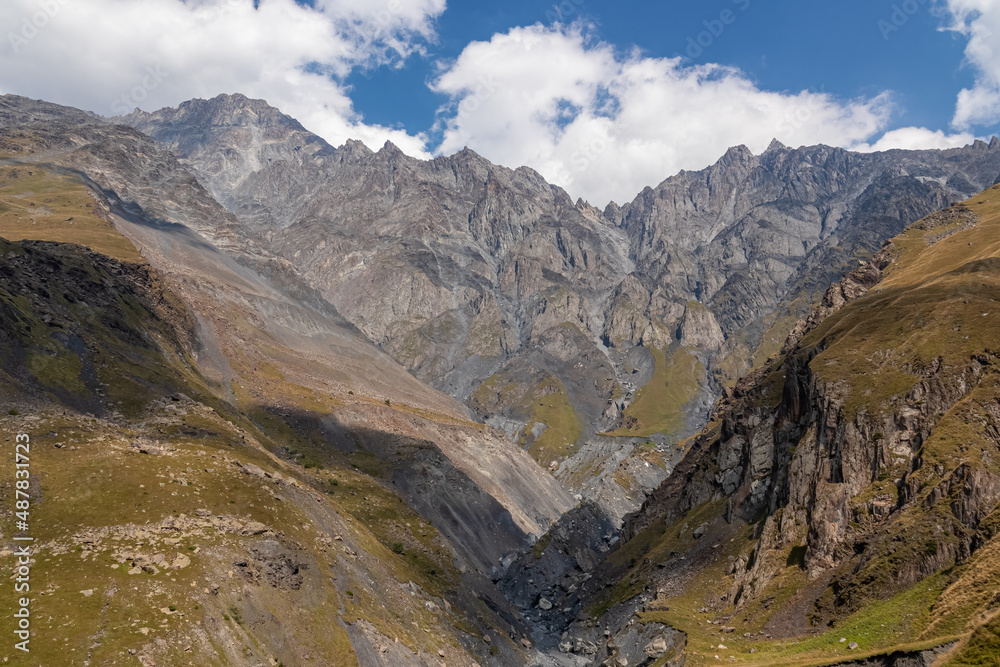 A panoramic view on the Kuro ridges in the Greater Caucasus Mountains in Georgia. There high slopes are barren and stony, lush pastures below.Clear and bright day.Khokh range. Stepantsminda.Adventure A panoramic view on the Kuro ridges in the Greater Caucasus Mountains in Georgia. There high slopes are barren and stony, lush pastures below.Clear and bright day.Khokh range. Stepantsminda.Adventure