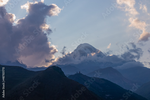 Distant view on Gergeti Trinity Church in Stepansminda, Georgia. The church is located the Greater Caucasian Mountain Range.Clouds are covering the snow-capped Mount Kazbegi in the back.Sunrise,sunset
