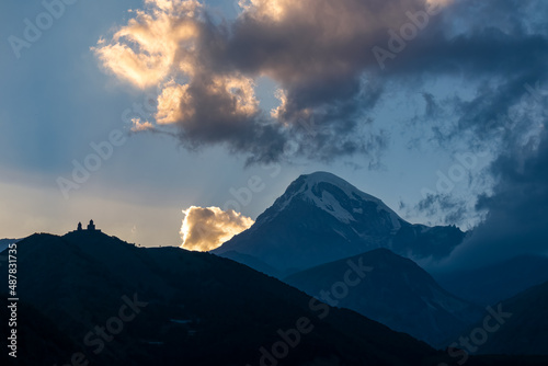 Distant view on Gergeti Trinity Church in Stepansminda  Georgia. The church is located the Greater Caucasian Mountain Range.Clouds are covering the snow-capped Mount Kazbegi in the back.Sunrise sunset