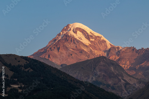 A panoramic morning view on Mount Kazbegi in the Greater Caucasus Mountains in Georgia. Clear sky over the snow-capped summit. Khokh range. Sunset, sunrise. Mystical. Adventure and discovery