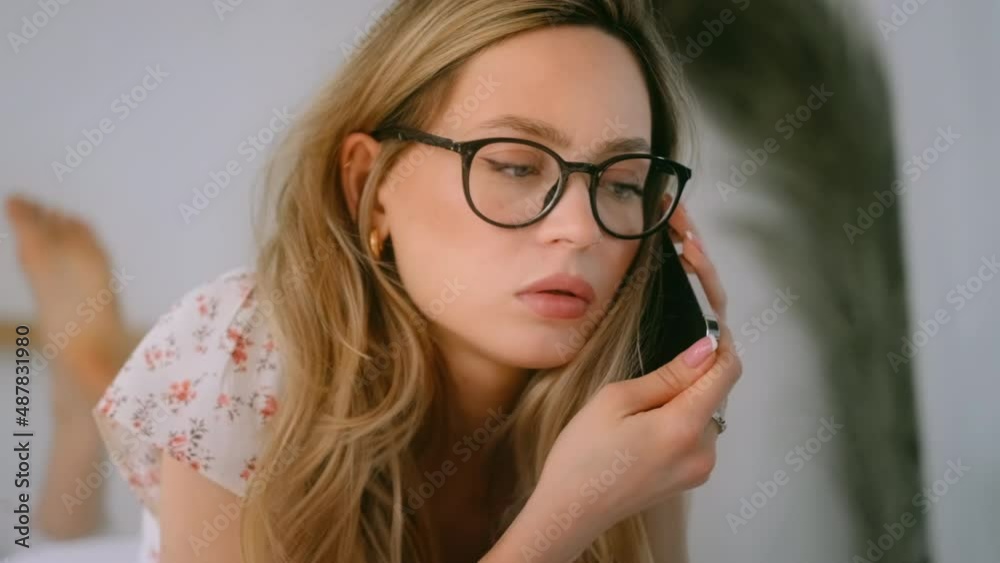 Serious young attractive caucasian woman in eyeglasses have important mobile conversation, lying on a bed. Serious young attractive caucasian woman in eyeglasses have important mobile conversation, lying on a bed.