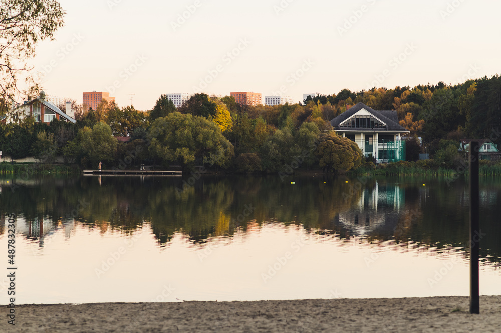 Autumn landscape near the lake. There are houses on the shore of the lake. You can see city houses in the distance.
